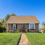 Brown rancher style house with green lawn. pathway to house in middle of the lawn.